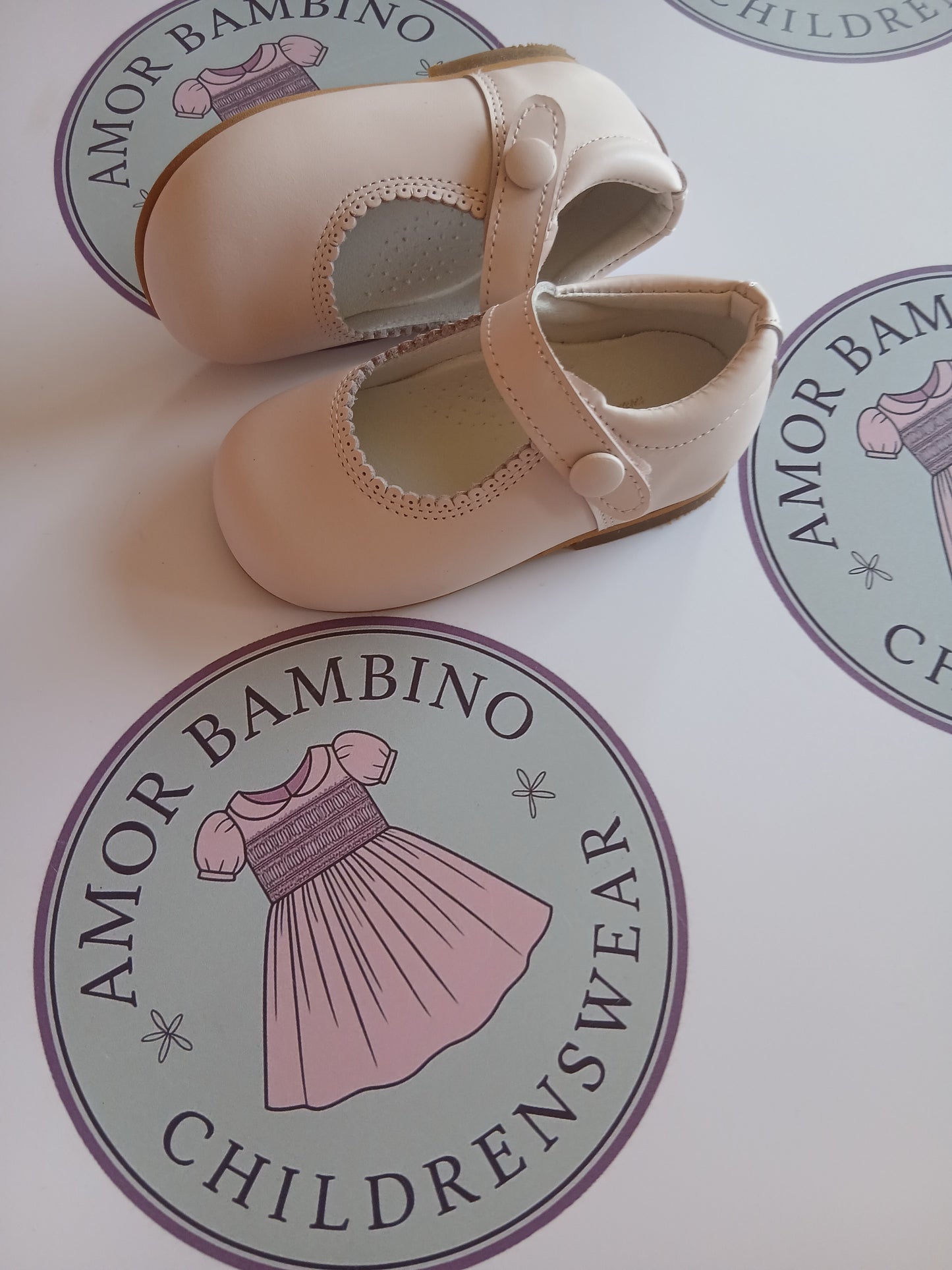 Girls Pink button matte shoes on amor Bambino childrenswear brand logo one shoe on its side.