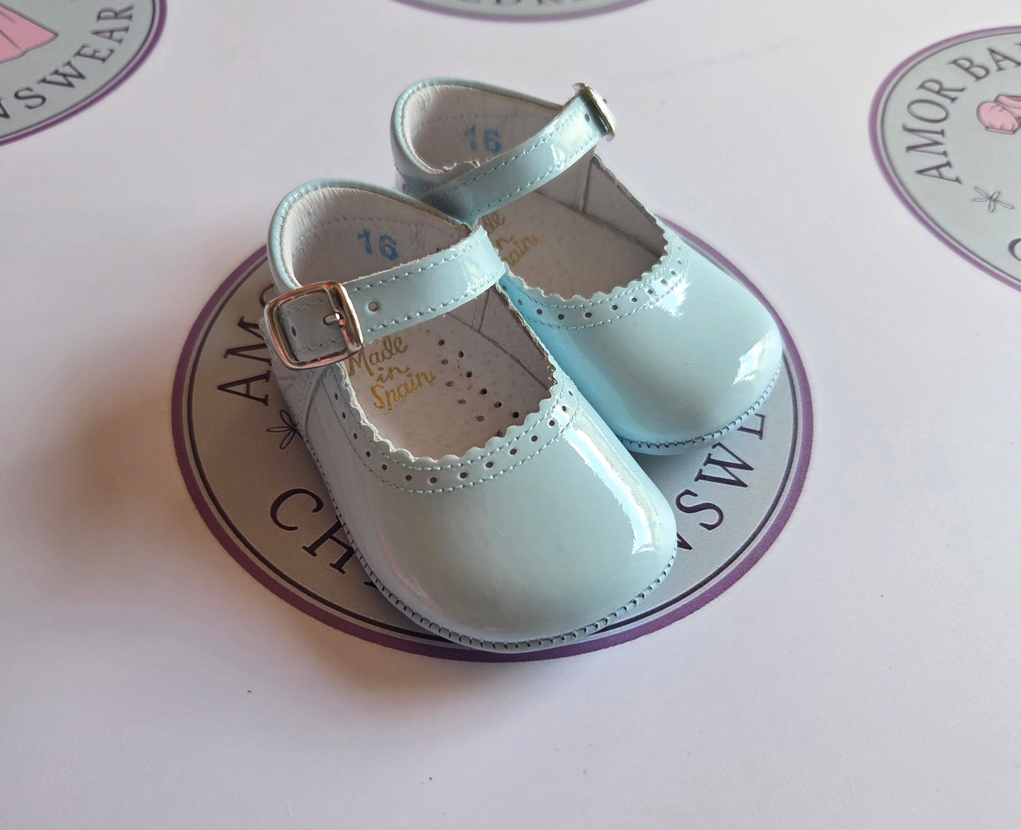 Girls baby blue patent leather mary jane pram buckle shoes on Amor Bambino childrenswear brand logo.