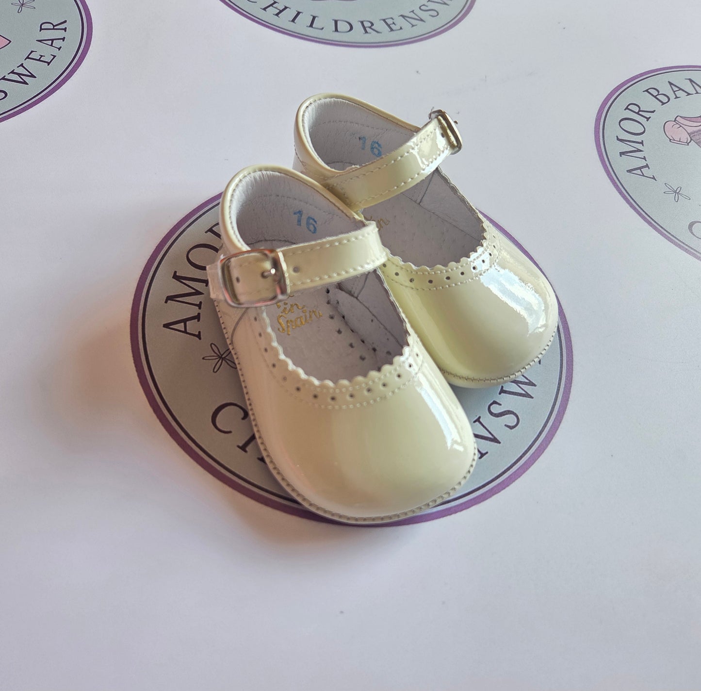 Girls cream patent leather mary jane pram buckle shoes on Amor Bambino childrenswear brand logo.