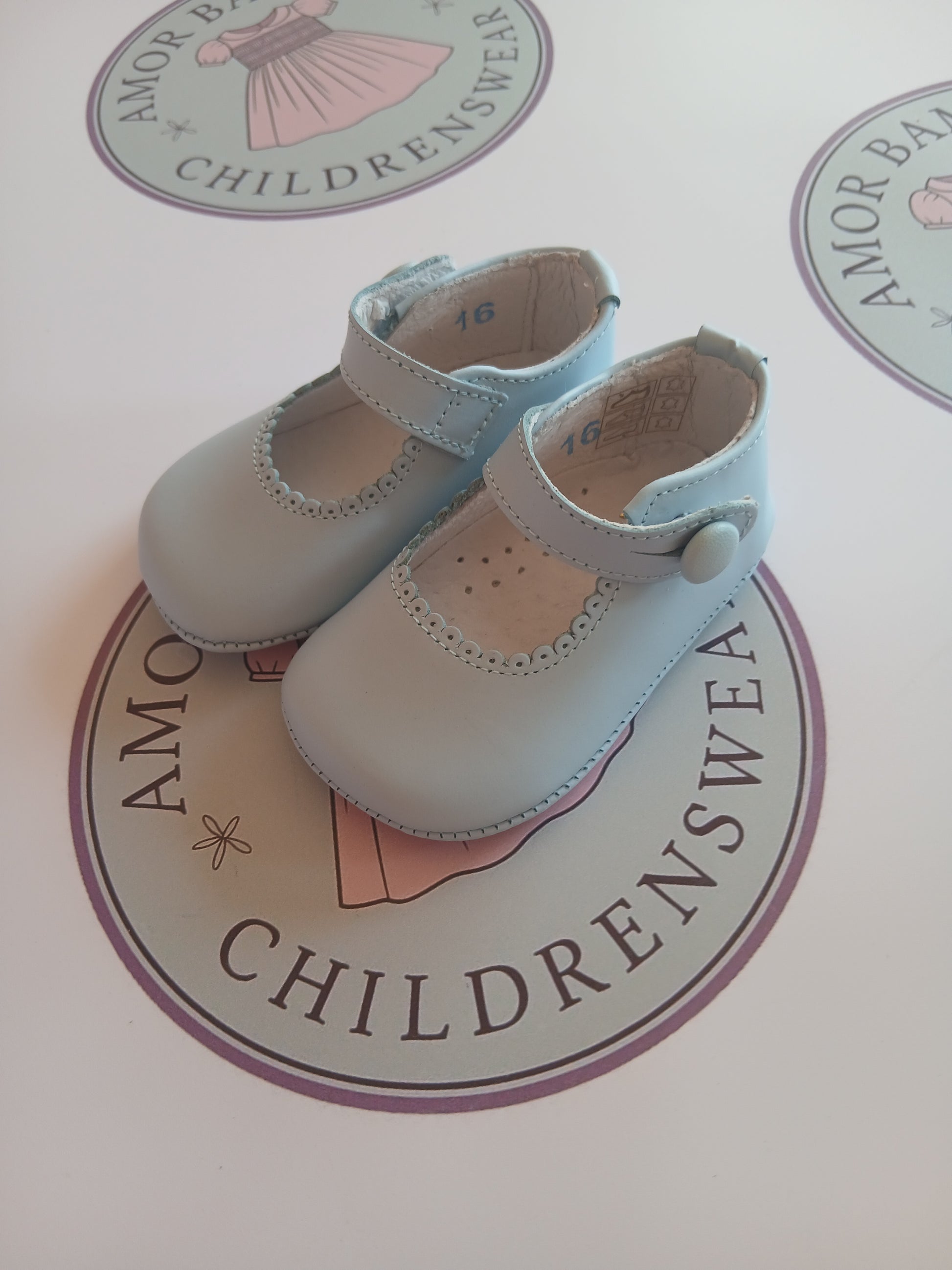 Girls baby blue button mary jane pram shoes on Amor Bambino childrenswear brand logo.